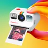 A hand holding a Polaroid Go camera, printing a photo. Produktbild-Vorschau