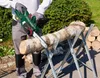 A person is using a cordless chainsaw to cut a log supported by a sawhorse outdoors. Produktbild-Vorschau