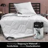 A bed with a white comforter and pillow, set up in a bedroom with a lamp and a vase. Produktbild-Vorschau