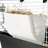 A close-up view of a white hay feeder filled with hay, attached to the side of a pet cage. Podgląd zdjęcia produktu