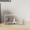 A clear acrylic display box containing three decorative items: a speckled sphere on a stand, a white rocket ship, and a crescent moon-shaped sculpture. The display box is placed on a wooden surface against a plain wall. Náhľad obrázku produktu