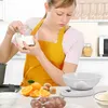 A woman in an apron is adding ingredients to a kitchen scale. Voir les images du produit