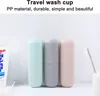 Three travel wash cups in pastel colors are displayed on a white surface, with a tube of toothpaste on the left and a toothbrush in a holder on the right. Produktbild-Vorschau
