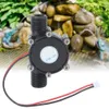 A black water turbine generator with red and black wires is shown in front of a decorative water feature with rocks and greenery. Náhled obrázku produktu