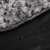A close-up view of a black, waterproof camping blanket with a fluffy gray lining. Water droplets are visible on the black surface. Produktbild-Vorschau