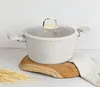 A beige pot with a glass lid and gold handle sits on a wooden board, with wheat stalks and a linen cloth nearby. Produktbild-Vorschau