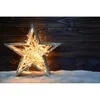 A star-shaped light decoration filled with fairy lights, placed on a snowy surface in front of a dark wooden background. Produktbild-Vorschau