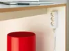 A close-up view of a white power strip with three outlets and a red cylindrical container on a desk. Produktbild-Vorschau