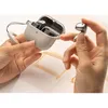 Hands holding a charging case for wireless earbuds, with one earbud being held by a finger. Produktbild-Vorschau