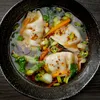 A close-up overhead view of dumplings in a broth with vegetables and chili flakes. Produktbild-Vorschau