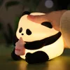 A hand is shown touching a glowing panda-shaped night light that is holding a pink baby bottle. Produktbild-Vorschau