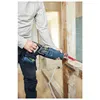 A person is using a reciprocating saw to cut through a wooden beam in what appears to be a renovation or construction site. Voir les images du produit