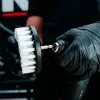 A gloved hand holds a drill brush attachment. Produktbild-Vorschau
