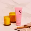 A pink tube of Alfaparf Milano Semi Di Lino Moisture Nutritive Leave-In Conditioner is placed on a marble surface next to two lit candles and some wooden hair styling tools. Produktbild-Vorschau