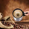 A hand holding a self-stirring mug filled with coffee, next to a burlap sack overflowing with coffee beans. Náhled obrázku produktu