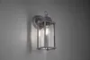 A wall-mounted outdoor lantern with a glass enclosure and a metal frame, attached to a light gray wall. Voir les images du produit