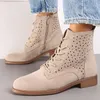 A pair of beige suede ankle boots with laser-cut floral patterns, worn with blue jeans. Voir les images du produit