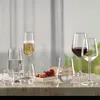 A collection of glassware, including wine glasses and tumblers, arranged on a marble surface with some fruit and nuts in the background. Anteprima dell’immagine prodotto