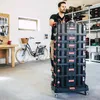 A man is pushing a stack of black storage boxes on a trolley in a workshop. Náhled obrázku produktu