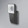 A dark gray LED floodlight with a sensor is mounted on a light gray wall. Produktbild-Vorschau