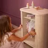 A young girl is opening a wooden doll wardrobe. Produktbild-Vorschau