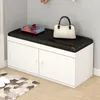 A white shoe cabinet with a black upholstered bench top, placed in a room with a rug and slippers on the floor. Anteprima dell’immagine prodotto