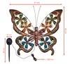 A decorative metal butterfly with colored glass inserts, shown with a solar panel stake and measurement indicators. Produktbild-Vorschau