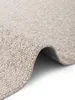 A close-up view of a cream-colored rug with a textured surface, showing the edge and a curled-up section. Voir les images du produit