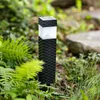 A solar garden light is shown in a natural outdoor setting, surrounded by greenery and rocks. Náhled obrázku produktu