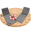 Two folded beach chairs on a sandy surface with a life preserver, sunglasses, and sunscreen. Produktbild-Vorschau