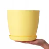A hand holding a yellow plant pot with a saucer. Náhled obrázku produktu