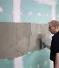 A person is applying adhesive to a wall with a trowel. Produktbild-Vorschau