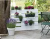 A white pallet planter filled with various flowers and plants, placed on a wooden deck next to a tree and a chair. Voir les images du produit