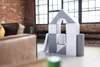 A set of soft building blocks arranged in a house shape in a room with brick walls and large windows. Produktbild-Vorschau
