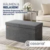 A grey storage bench in a modern living room setting with a vase of flowers and a chair in the background. Anteprima dell’immagine prodotto