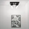 A black ceiling light fixture with four adjustable spotlights is mounted on a white ceiling. Below the light fixture, a framed piece of abstract art with circular patterns hangs on a white wall. Voir les images du produit