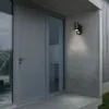 An outdoor wall lamp with a motion sensor is mounted on a concrete wall next to a modern gray door and window. Produktbild-Vorschau