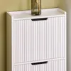 A close-up view of a white shoe cabinet with fluted doors and a dark handle. A glass vase with dried flowers is on top. Náhľad obrázku produktu