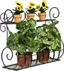 A black metal wall-mounted plant stand holding two tiers of plants. The top tier has three small potted sunflowers, and the bottom tier has two larger potted plants with green leaves. Náhľad obrázku produktu