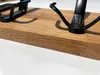 A close-up of two black metal hooks mounted on a wooden plank. Produktbild-Vorschau