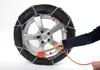 A person's hand is shown attaching snow chains to a car tire. Produktbild-Vorschau