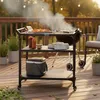 A BBQ grill cart is set up on a wooden deck with food being grilled. Anteprima dell’immagine prodotto