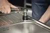 A person is using a socket wrench to tighten a fitting on a stainless steel sink. Produktbild-Vorschau