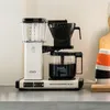 A white Moccacoffee machine with a glass carafe filled with coffee sits on a countertop. Produktbild-Vorschau