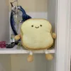 A plush toy shaped like a slice of toast sits on a shelf next to a decorative sculpture. Náhľad obrázku produktu