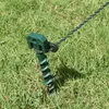 A close-up of a green screw-in ground stake with a black clip holding a twisted wire, embedded in grass. Náhľad obrázku produktu