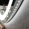 A close-up view of a lighted mirror with LED lights along the edge, mounted on a textured wall. Produktbild-Vorschau