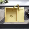 A golden sink with a faucet is shown from a top-down view, placed on a gray countertop. There are plants in the background. Produktbild-Vorschau