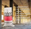 A white asbestos bag is shown in a construction site with concrete pillars and debris. Produktbild-Vorschau