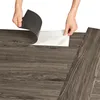 Hands peeling back the protective backing from a vinyl flooring plank to reveal the adhesive side. Produktbild-Vorschau